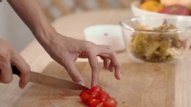 Close up hands holding a knife preparing a contented meal. Sliced tomatoes and other vegetables on the glass dish.