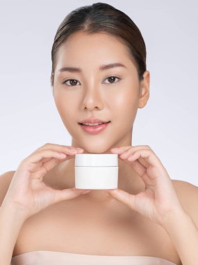 Gorgeous woman smiling holding mockup product for advertising text place, light grey background. Concept of healthcare for skin, beauty care product for advertising.