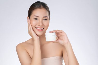 Gorgeous woman smiling holding mockup product for advertising text place, light grey background. Concept of healthcare for skin, beauty care product for advertising.