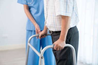 Physiotherapist assists contented senior man on folding walker. Recuperation for elderly, seniors care, nursing home.