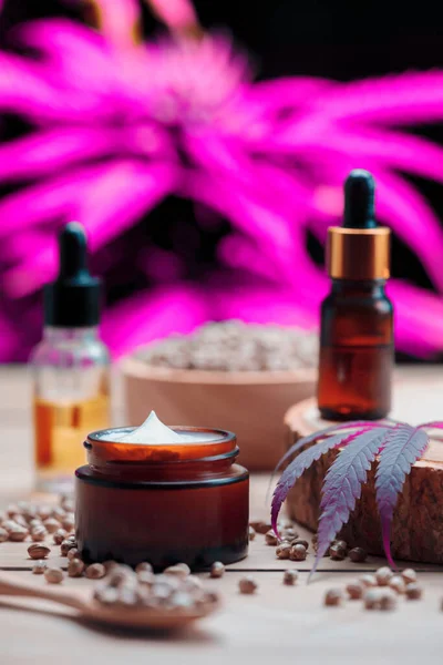 Cannabis and cosmetic concept features with set of CBD oil bottles, cream jar, and wooden bowl of hemp seeds. Legalized cannabis for skincare products.