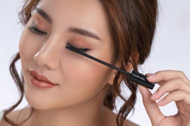 Closeup gorgeous young woman putting black mascara on her long eyelashes with brush. Beauty cosmetic concept. Female model with perfect skin.