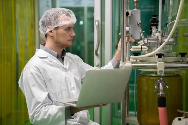 Eczacı bilimadamı CBD yağ çıkarıcısından bilgi kaydetmek için dizüstü bilgisayar ve tıbbi esrar ürünleri üretmek için kullanılan bilimsel bir makine kullanıyor..
