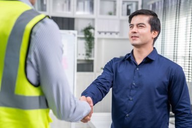 An engineer with a protective vest handshake with an investor in his office. Following a successful meeting, employee and employer form a partnership.