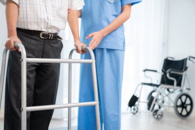 Physiotherapist assists contented senior man on folding walker. Recuperation for elderly, seniors care, nursing home.