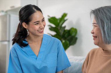 A caregiver rest her hands on the shoulders of a contented senior patient while she sitting on the sofa at home.