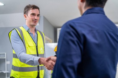 An engineer with a protective vest handshake with an investor in his office. Following a successful meeting, employee and employer form a partnership.