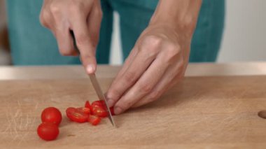 Close up hands holding a knife preparing a contented meal. Sliced tomatoes and other vegetables on the glass dish.
