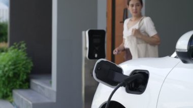 Evinde şarj edilen elektrikli bir araçla işten yeni dönen modern bir kadının ilerici yaşam tarzı. Elektrikli araç, sürdürülebilir temiz enerjiyle çalışıyor..