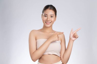 Photo of a gorgeous woman in a concept of empty space for beauty care product on isolated light gray background. Skincare product, model uses hand to create empty space for commercial.