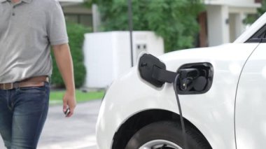 İlerici adam evindeki elektrikli aracın aküsüne emisyonsuz güç bağlantısı kuruyor. Elektrikli araç elektrik istasyonundan EV araba aküsüne kabloyla şarj oluyor.
