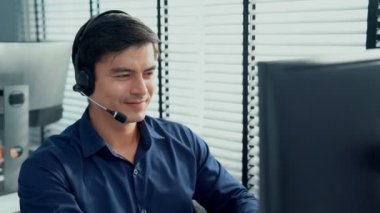 Young competent asian male call center agent working at his computer while simultaneously speaking with customers. Concept of an operator, customer service agent working in the office with headset.