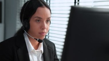 Competent african american female operator working on computer and while talking with clients. Concept relevant to both call centers and customer service offices.
