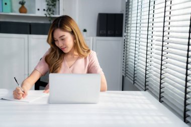 A young Asian female employee sitting at her desk in her office, sitting at desktop in workstation.