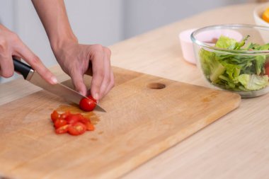 Close up hands holding a knife preparing a contented meal. Sliced tomatoes and other vegetables on the glass dish.