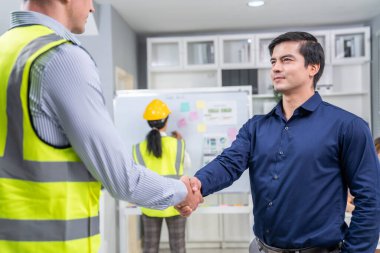 An engineer with a protective vest handshake with an investor in his office. Following a successful meeting, employee and employer form a partnership.