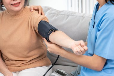An elderly woman with a contented life having a blood pressure check by her caregiver at home with a smiley face.