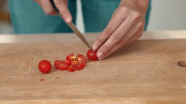 Close up hands holding a knife preparing a contented meal. Sliced tomatoes and other vegetables on the glass dish.