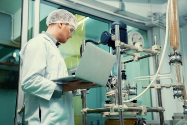 CBD yağ çıkarıcısının yanında dizüstü bilgisayarla çalışan eczacı bilim adamı ve tıbbi esrar ürünleri üretmek için kullanılan bilimsel bir makine.