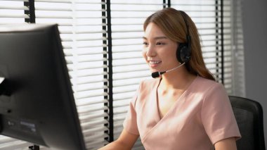Competent female operator working on computer and while talking with clients. Concept relevant to both call centers and customer service offices.