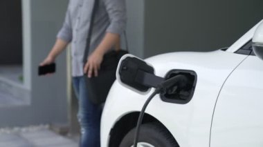 Adamın biri evinde elektrikli araç şarj aletinin fişini çekiyor. İlerici bir yaşam tarzında elektrikli araçların kullanımı, temiz ve sağlıklı bir çevreye katkıda bulunur..