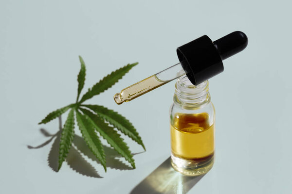 Комплект марихуаны с продуктом CBD масла на стеклянной бутылке с крышкой капельницы, листья конопли и сухой бутон, листья конопли и бутон расположены на пустом фоне. Концепция продукта конопли.