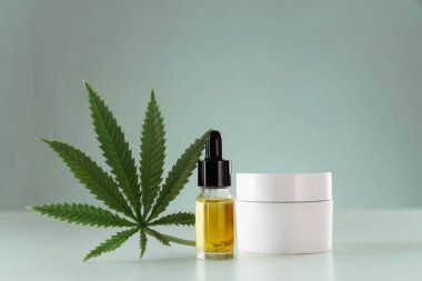 Marihuana yaprağının CBD yağına damıtılması kavramı dermatolojik amaçla beyaz model nemlendirici konteynır ile. Copyspace ve reklam için esrar ve cilt ürünleri.