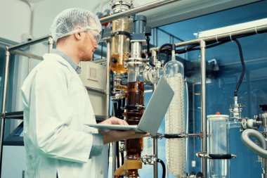 CBD yağ çıkarıcısının yanında dizüstü bilgisayarla çalışan eczacı bilim adamı ve tıbbi esrar ürünleri üretmek için kullanılan bilimsel bir makine.
