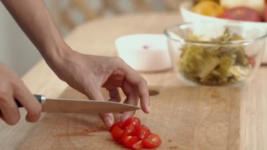 Close up hands holding a knife preparing a contented meal. Sliced tomatoes and other vegetables on the glass dish.