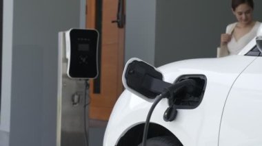 İlerici ebeveynler kızlarını okuldan alırken elektrikli araba ve yenilenebilir enerji kavramını kullandılar, evdeki EV otomobil için şarj istasyonu. Alternatif eko taşımacılığı.