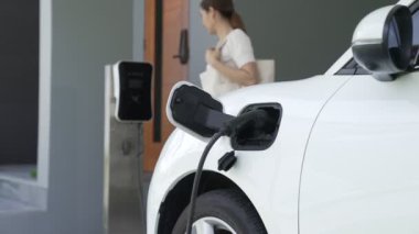 Bir kadın evinde elektrikli araç şarj aletinin fişini çekiyor. İlerici bir yaşam tarzında elektrikli araçların kullanımı, temiz ve sağlıklı bir çevreye katkıda bulunur..