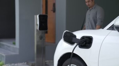 Adamın biri evinde elektrikli araç şarj aletinin fişini çekiyor. İlerici bir yaşam tarzında elektrikli araçların kullanımı, temiz ve sağlıklı bir çevreye katkıda bulunur..
