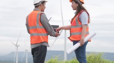 Erkek ve kadın mühendisler kırsal kesimdeki bir tepenin tepesinde ya da dağda rüzgar çiftliğinde çalışıyorlar. Yenilenebilir ve sürdürülebilir enerjinin gelecekteki üretimi için yenilikçi idealler.