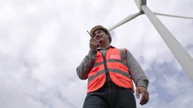 Gökyüzü arka planına sahip bir rüzgar türbini üzerinde çalışan mühendis. Yenilenebilir ve sürdürülebilir enerjinin gelecekteki üretimi için yenilikçi bir ideal. Rüzgar türbininden enerji üretimi.