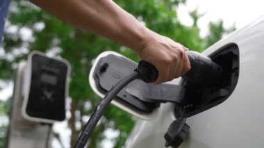 İlerici adam elektrikli aracına elektrik kablosu takıyor. Ev şarj istasyonundan EV arabası. Çevreyi korumak için temiz ve yenilenebilir enerji kullanan elektrikli bir araba. Çevre dostu otomobil.
