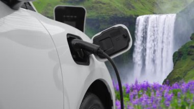 Elektrikli araba, doğal ortam, şelale ve akış arkaplanındaki şarj istasyonundan enerji yüklüyor. Yenilenebilir enerji kaynaklı EV otomobillerin enerji sürdürülebilirliği kavramı.
