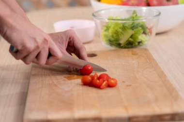 Close up hands holding a knife preparing a contented meal. Sliced tomatoes and other vegetables on the glass dish.