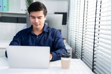 Competent male employee sits at his desk with a cup of coffee. Modern employee working with a drink, recreation during working hours, caffeine for office workers.
