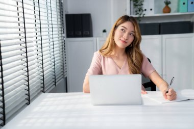 A young Asian female employee sitting at her desk in her office, sitting at desktop in workstation.