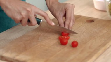 Close up hands holding a knife preparing a contented meal. Sliced tomatoes and other vegetables on the glass dish.
