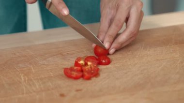 Close up hands holding a knife preparing a contented meal. Sliced tomatoes and other vegetables on the glass dish.