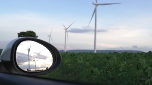 風力発電機からのグリーン 再生可能エネルギーを利用した充電ステーションにおいて 電気自動車のサイドミラーに反射する風力発電機の先進的な未来エネルギーインフラの概念 — ストック動画