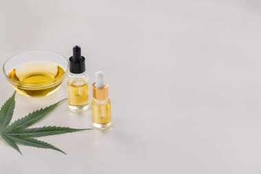 Cam kase ve bir şişe CBD yağı, kenevir tomurcuğu ve kenevir yaprağı beyaz arka planda gösterilir. Esrardan yasallaştırılmış yağ özü kavramı.