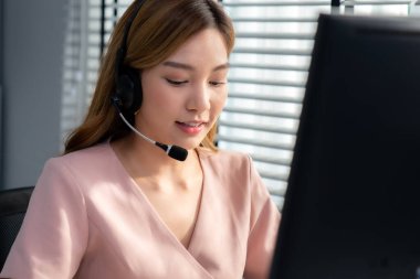 Competent female operator working on computer and while talking with clients. Concept relevant to both call centers and customer service offices.