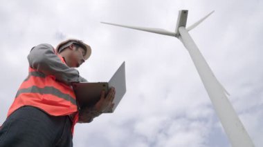 Gökyüzü arka planına sahip bir rüzgar türbini üzerinde çalışan mühendis. Yenilenebilir ve sürdürülebilir enerjinin gelecekteki üretimi için yenilikçi bir ideal. Rüzgar türbininden enerji üretimi.