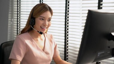 Competent female operator working on computer and while talking with clients. Concept relevant to both call centers and customer service offices.