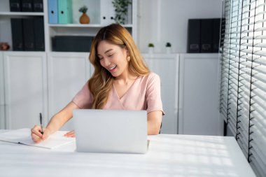 A young Asian female employee sitting at her desk in her office, sitting at desktop in workstation.