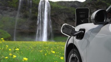 Elektrikli araba, doğal ortam, şelale ve akış arkaplanındaki şarj istasyonundan enerji yüklüyor. Yenilenebilir enerji kaynaklı EV otomobillerin enerji sürdürülebilirliği kavramı.