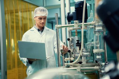 CBD yağ çıkarıcısının yanında dizüstü bilgisayarla çalışan eczacı bilim adamı ve tıbbi esrar ürünleri üretmek için kullanılan bilimsel bir makine.