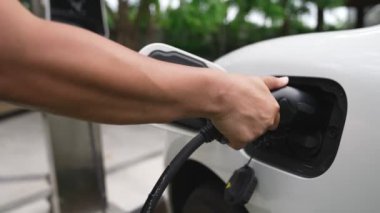 İlerici adam elektrikli aracına elektrik kablosu takıyor. Ev şarj istasyonundan EV arabası. Çevreyi korumak için temiz ve yenilenebilir enerji kullanan elektrikli bir araba. Çevre dostu otomobil.